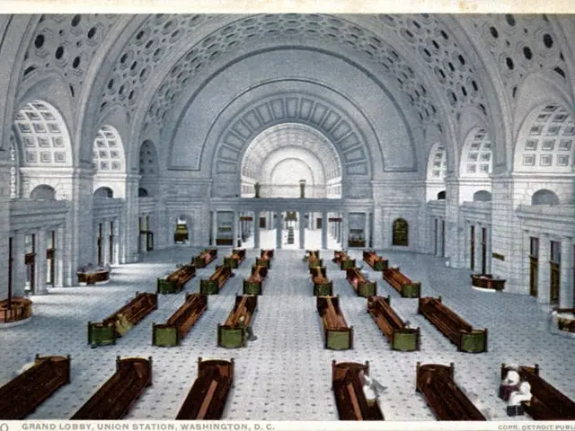 The image shows an old photo of a large room with many benches, pillars, arches, and windows. At...