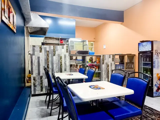 The image shows a restaurant with blue chairs and tables in it, a refrigerator on the right side, a...