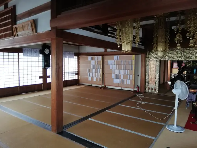 The image shows a room with tatami mats on the floor, a table fan, a carpet, a fire extinguisher,...