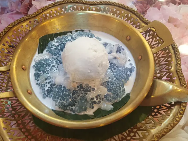 The image shows a bowl of ice cream sitting on top of a gold plate, with a spoon beside it. On the...