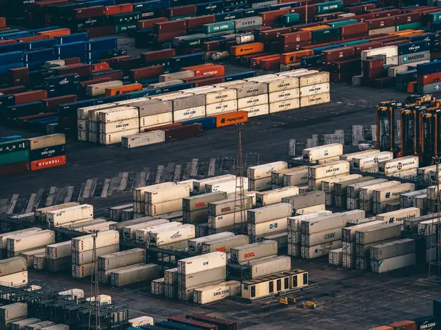 The image shows an aerial view of a large number of shipping containers stacked on top of each...