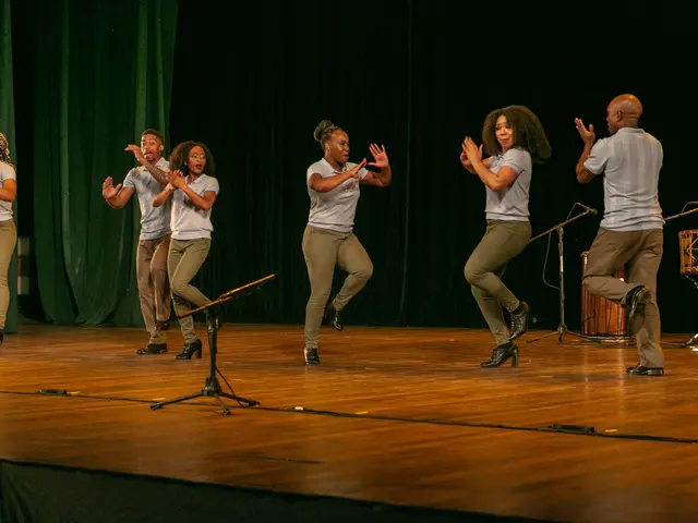 The image shows a group of people standing on top of a stage, clapping their hands in celebration....