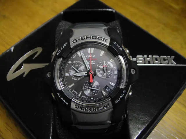 The image shows a black Casio G-Shock GBA-800-1A watch sitting atop a black box on a brown table....