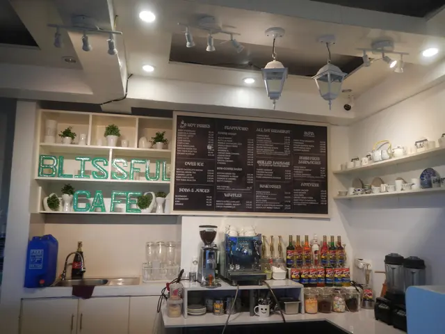 The image shows a blissful cafe with a counter top and a menu on the wall. On the counter top there...