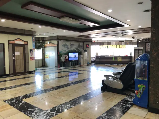 The image shows the lobby of a hotel with a large marble floor, electric lights to the roof, doors,...
