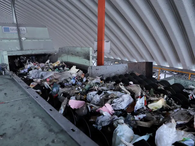 The image shows a large pile of trash sitting on top of a conveyor belt, with a machine in the...