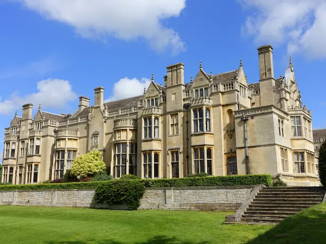 The image shows a large building with a green lawn in front of it, surrounded by trees, plants, and...