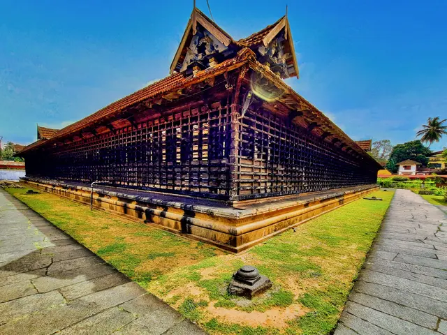 The image shows a large building with a lot of windows in the middle of it, surrounded by grass and...