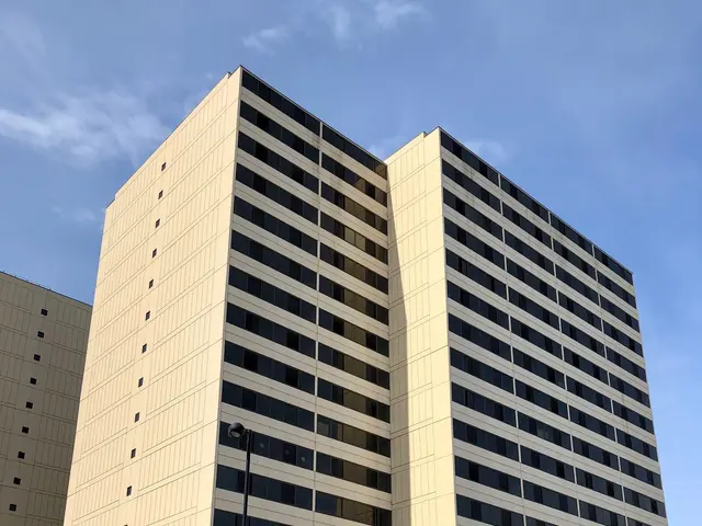 The image shows a tall building with many windows on the side of it, situated on the corner of a...