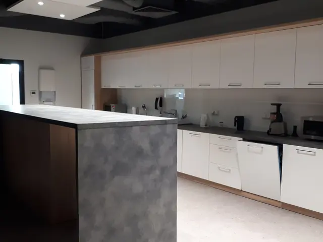 The image shows a kitchen with white cabinets and a large island in the middle of it. On the island...