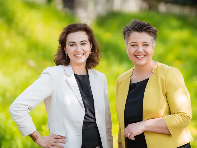 The image shows two women standing next to each other in a field, both wearing black and yellow...