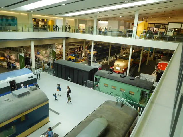 The image shows a large room filled with lots of different types of trains, people, railings,...