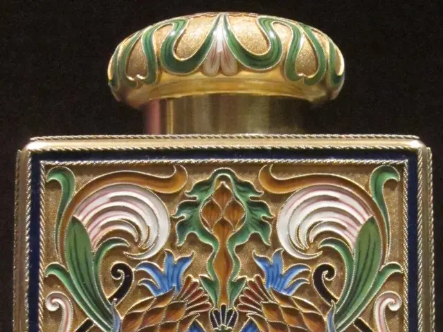 The image shows a gold and enamel perfume bottle with a floral design on it, set against a dark...