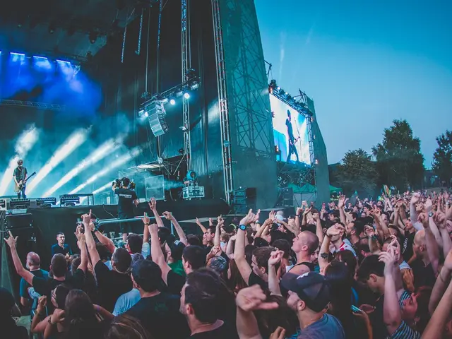 The image shows a crowd of people at a music festival with their hands in the air, gathered around...