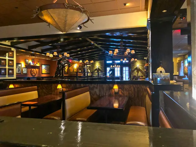 The image shows the interior of a restaurant with tables and booths, sofas, lamps, a platform with...