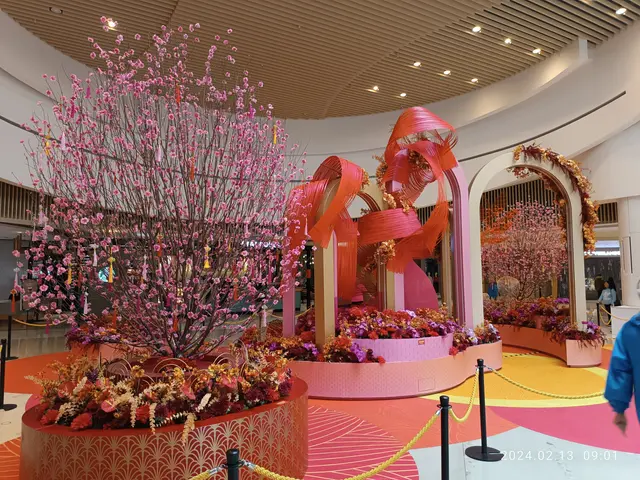 The image shows a man walking through a large room filled with lots of pink flowers, surrounded by...
