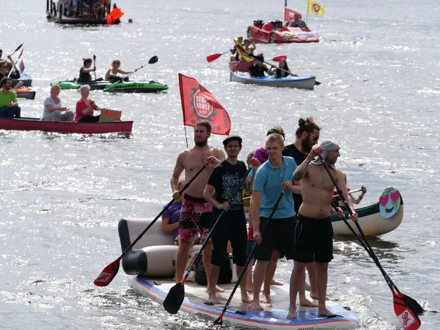 The image shows a group of people standing on top of a paddle board in the water, with some of them...