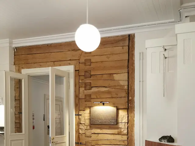 The image shows a living room with a cozy atmosphere, featuring a sofa with cushions, chairs with...