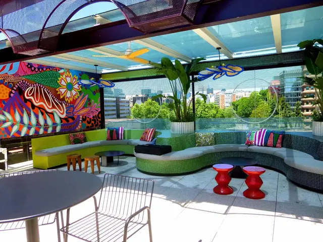 The image shows a patio with a colorful couch, tables and chairs, cushions on the sofa, stools,...