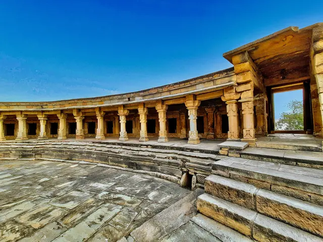 The image shows a large stone building with many pillars and steps in the middle of it, surrounded...