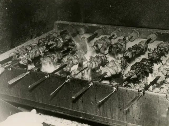 The image shows a black and white photo of a person cooking kebabs on a grill, with their hand...