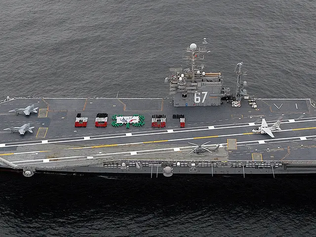 The image shows an aerial view of an aircraft carrier in the ocean, with aeroplanes, vehicles, and...