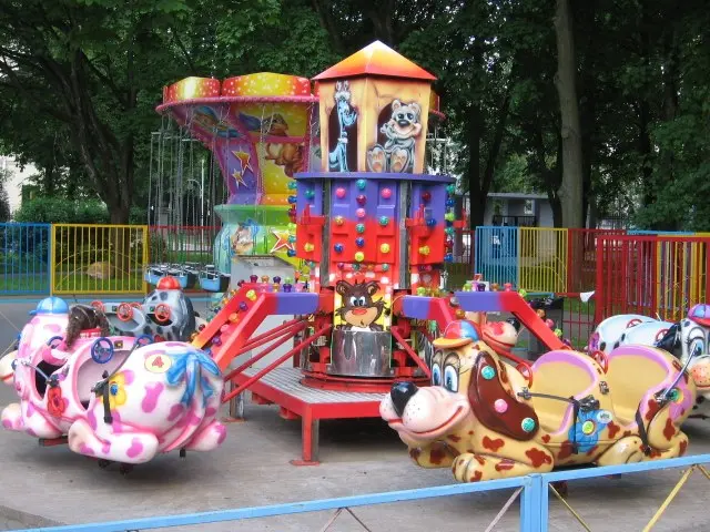 The image shows an amusement park with a carousel in the middle of it, surrounded by a railing and...