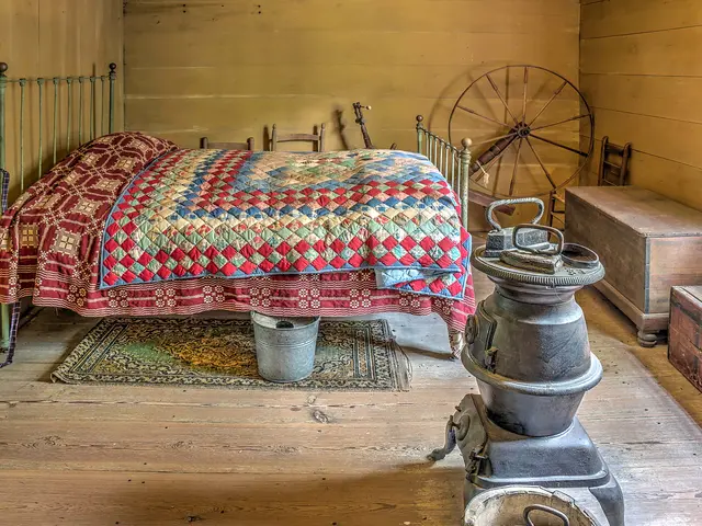 The image shows a bedroom with a bed covered in a quilt, two buckets on the floor, a wooden box, a...