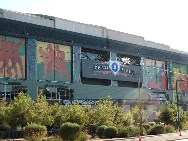 In the image there is a baseball park and in front of that there are many plants and trees.
