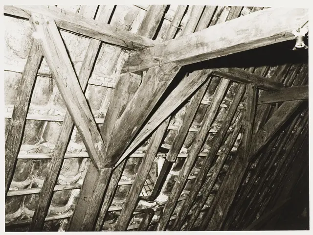 The image shows a black and white photo of an attic with wooden beams and a wall in the background....