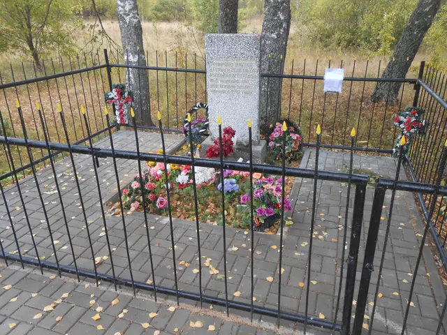 The image shows a memorial in the middle of a park surrounded by a metal fence, with flower...