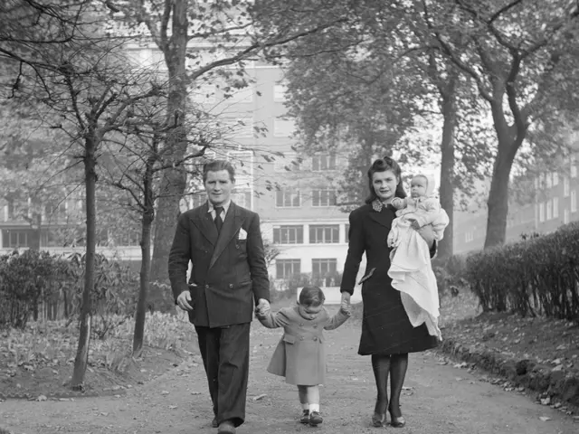 The image shows a black and white photo of a family walking down a path in a park. The man and...