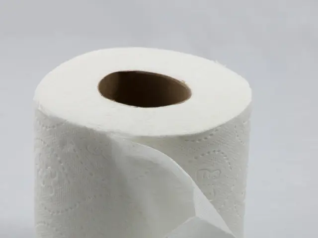 The image shows a roll of toilet paper sitting on top of a white surface. The paper roll is...
