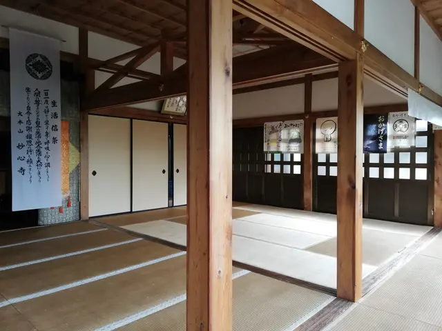 The image shows a room with tatami mats on the floor, wooden pillars, banners with text and...