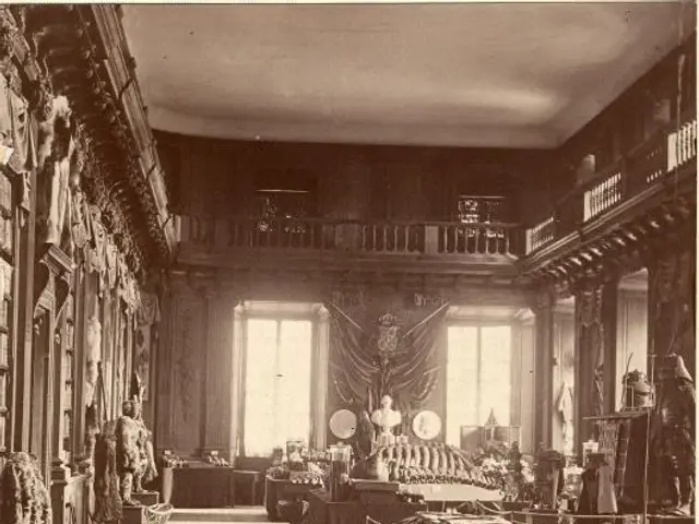 The image shows an old black and white photo of a room filled with lots of tables and chairs,...
