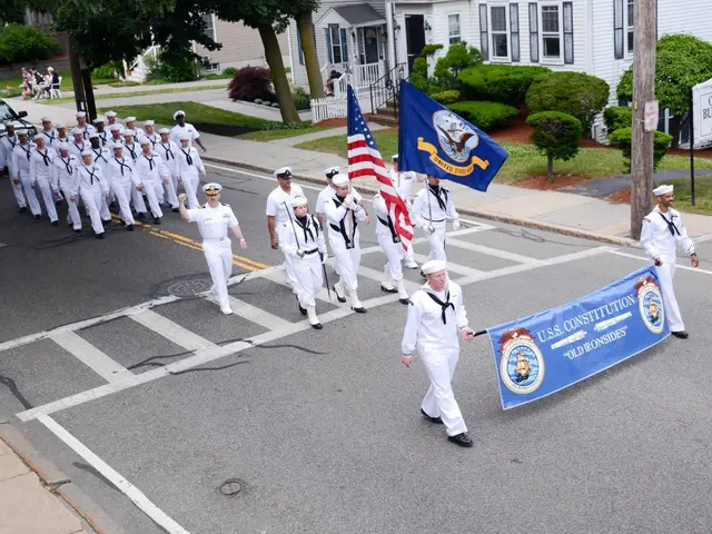 The image shows a group of people in white uniforms marching down a street, with some of them...