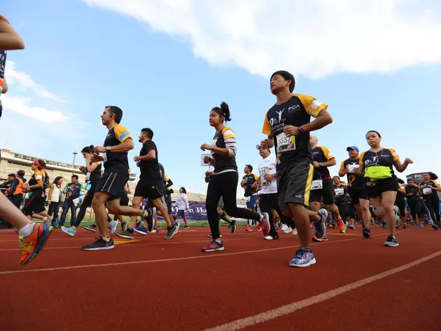 The image shows a group of people running on a track, with a crowd of people standing on the right...