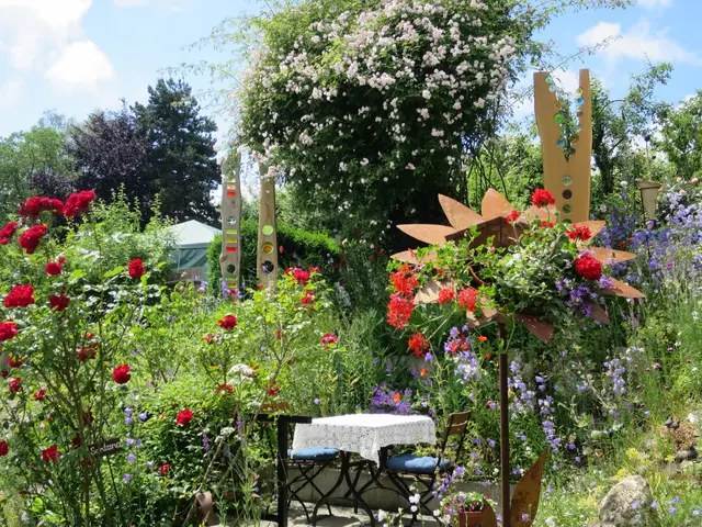 The image shows a garden filled with lots of colorful flowers and plants, with a table and chairs...