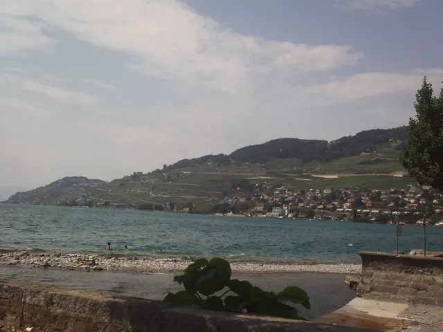 The image shows a picturesque view of a body of water with people swimming in it, surrounded by...
