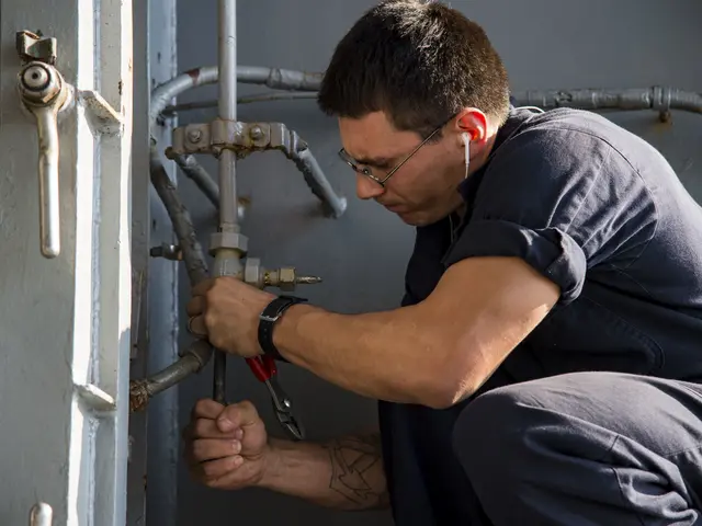 The image shows a plumber wearing glasses, a watch, and earphones, holding a tool and fixing a pipe...
