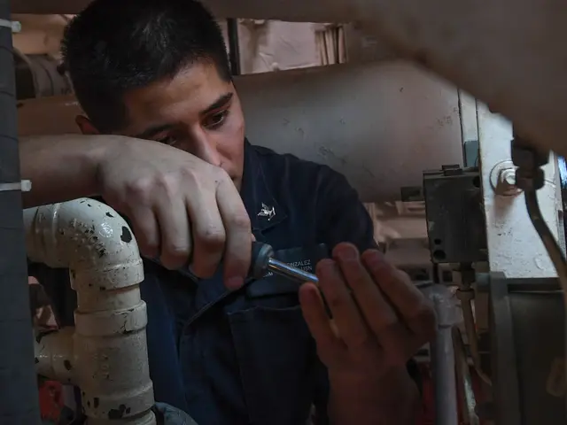 The image shows a man working on a pipe in a room, holding a tool in his hand. He appears to be a...