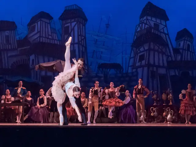 The image shows a couple of ballet dancers performing on a stage in front of a crowd of people...